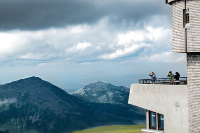 People standing on mountain against cloudy sky