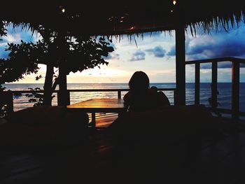 Silhouette woman sitting on beach against sky during sunset