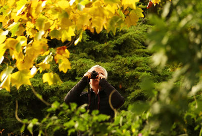 Man with camera seen through plants outdoors