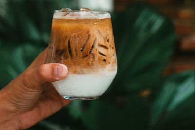 Hand hold iced latte coffee in a glass with cream on bottom . cold summer drink background