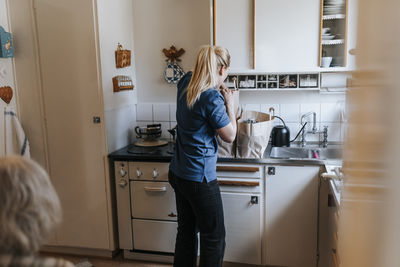 Female caregiver unpacking groceries while standing in kitchen at home