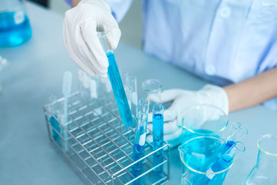 Midsection of scientist holding blue chemical in test tube at laboratory