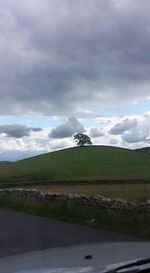 Road passing through field against cloudy sky