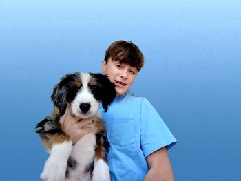 Young generation z teenager holding his dog on blue background.