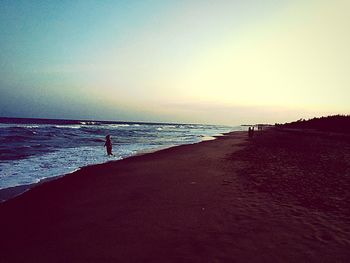 People on beach against sky during sunset