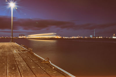 Illuminated pier over river against sky at night