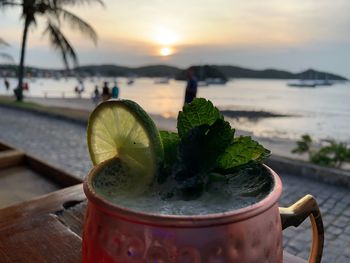 Close-up of drink against sea at sunset