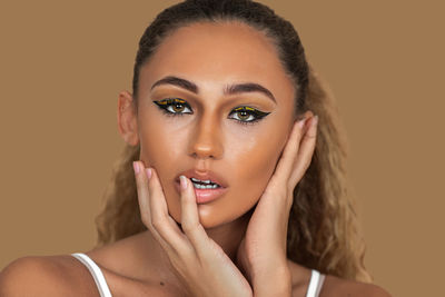 Portrait of young woman applying make-up against pink background