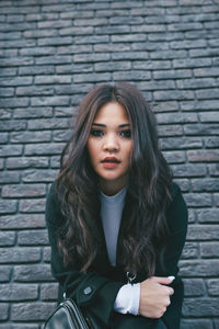 Portrait of a beautiful young woman standing against brick wall