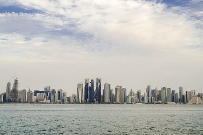 Sea by modern buildings against sky in city