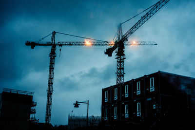 Low angle view of cranes at construction site against sky