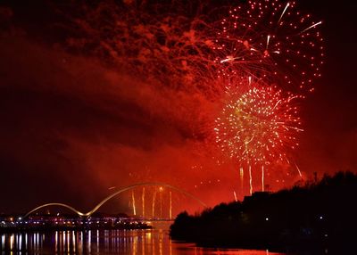 Firework display over bridge against sky at night