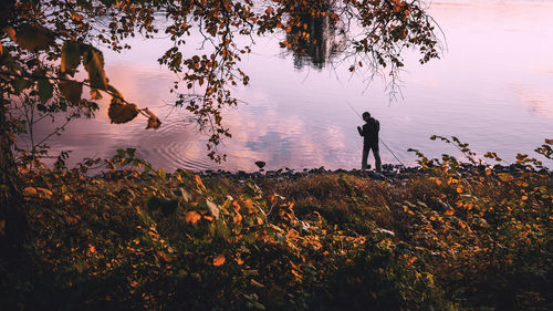 Silhouette man standing by lake against sky during sunset