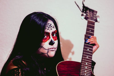 Close-up portrait of young woman with face paint holding guitar at home