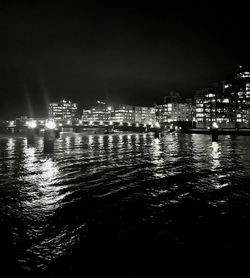 Illuminated city by sea against sky at night