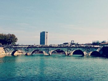 Bridge over river by buildings against sky