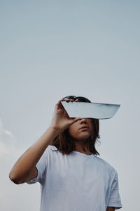 Low angle view of woman holding mirror against sky