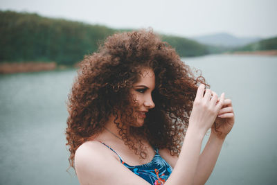 Young woman with curly hair standing against lake