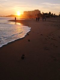 People on beach against sky during sunset