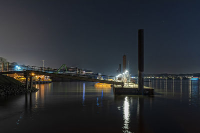 Illuminated bridge by river against sky at night