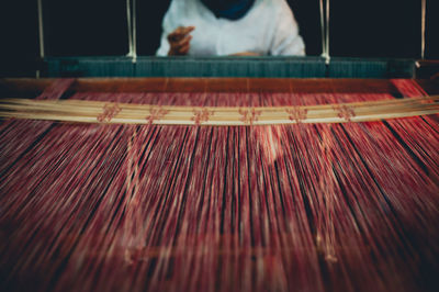 Midsection of woman weaving loom at factory
