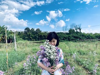 Young woman with bouquet standing on field against sky
