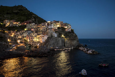 Illuminated houses on rock formation at manarola by sea against clear sky
