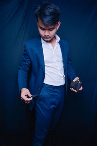 Young businessman looking at empty pocket while standing against blue background