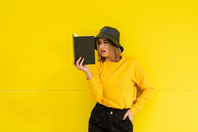 Close-up of a smiling young caucasian woman on a yellow background holding a book