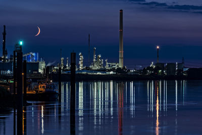 Illuminated buildings by river against sky at night