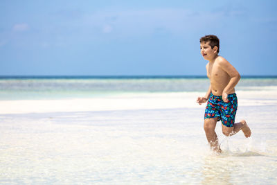 Rear view of shirtless man standing at beach against sky