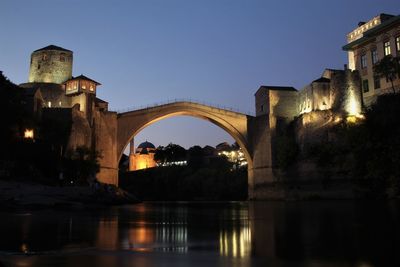 Bridge over river by illuminated buildings against clear sky