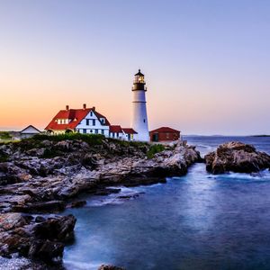Lighthouse by sea and buildings against sky during sunset