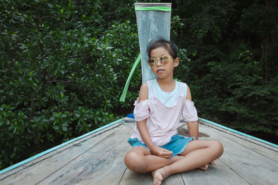 Full length of girl wearing sunglasses sitting on boat deck against tree