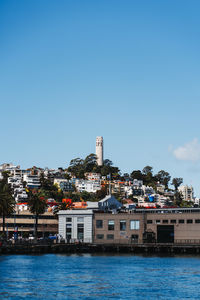 Buildings by river against clear blue sky