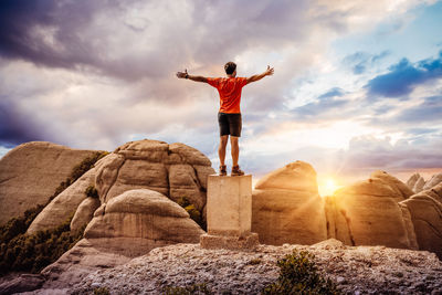 Rear view of man standing on rock against sky