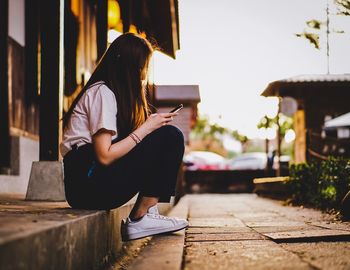 Side view of woman sitting on footpath in city