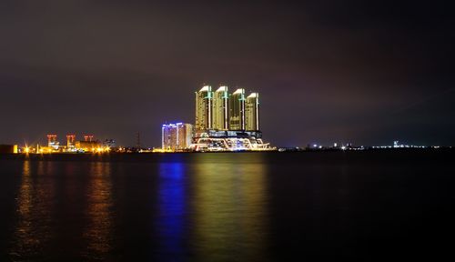 Illuminated city by sea against sky at night