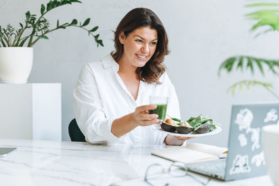 Young nutritionist in white with healthy food at office. doctor communicates with patient online