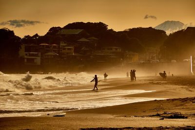 Silhouette people on beach against sky during sunset