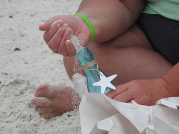 Cropped hand putting sand in bottle at beach