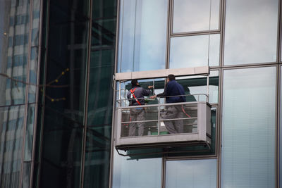 Low angle view of window washers cleaning glass building