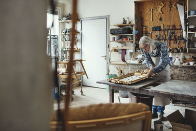 Senior female owner working on carved product at workshop