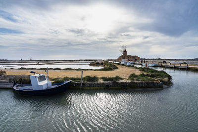 Traditional fishing boat near salt museum windmill at saline dello stagnone, marsala, sicily, italy