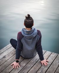 Rear view of man sitting on wooden pier