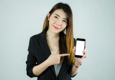 Portrait of smiling young woman using phone against white background