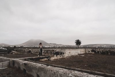 Rear view of woman standing at old ruins against sky