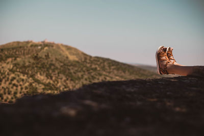 Low section of woman on mountain against clear sky