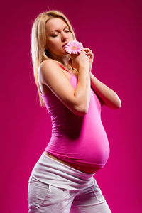 Pregnant woman holding flower standing against pink background