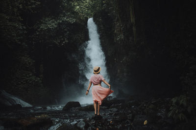 Rear view of woman standing against waterfall